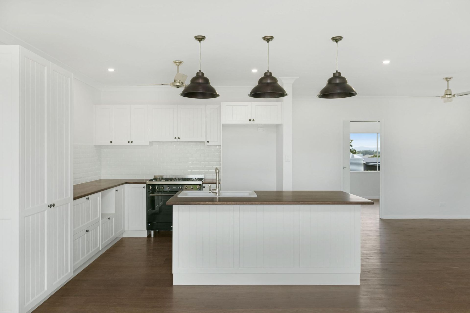 An Empty Kitchen With White Cabinets and a Large Island — Ashlee Jones Homes in Gordonvale, QLD