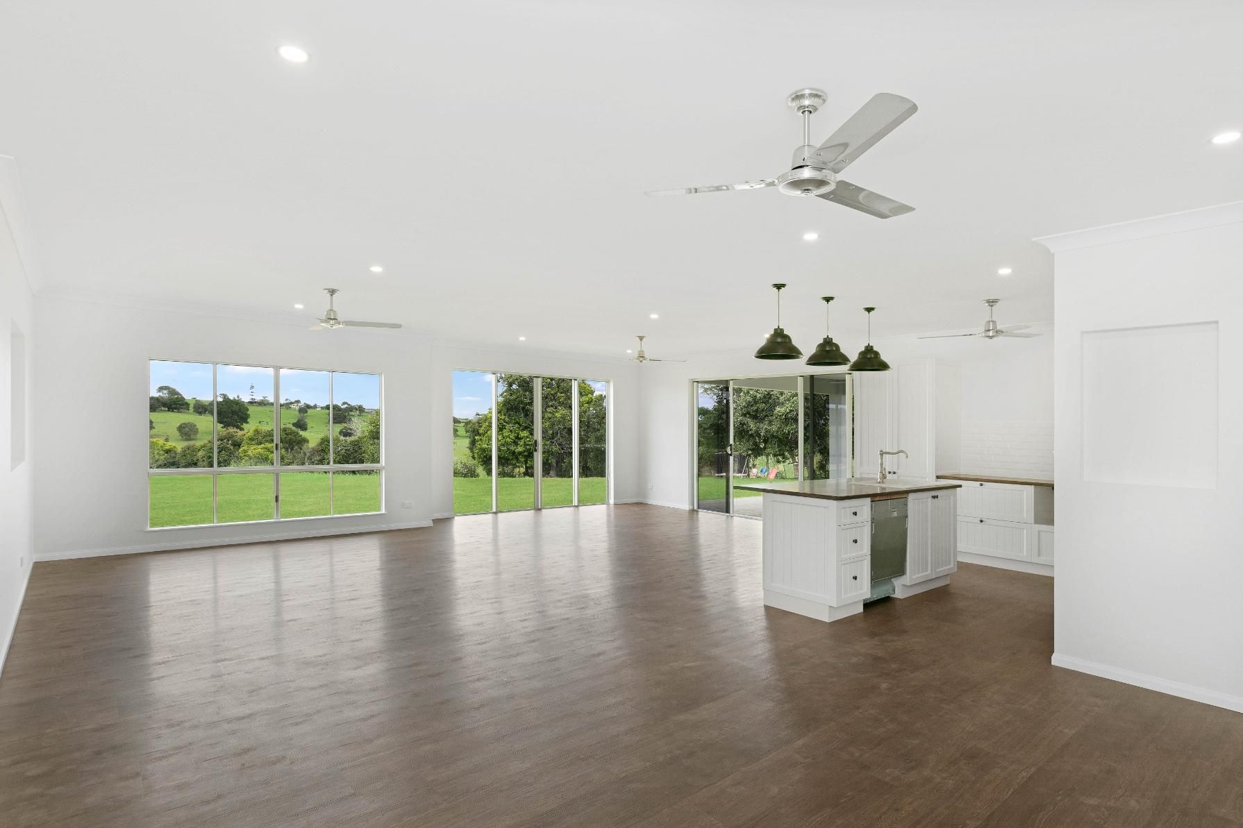 A Large Empty Room With Hardwood Floors and a Ceiling Fan — Ashlee Jones Homes in Gordonvale, QLD