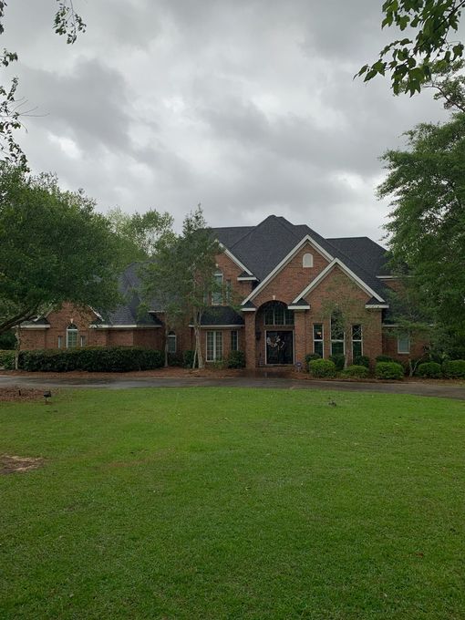 Brick house with black roof and large lawn under cloudy sky.