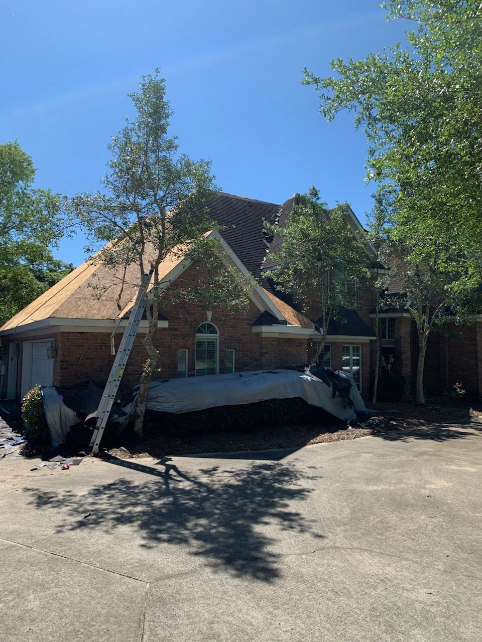 A brick home damaged by a fallen tree. The roof is partially collapsed with debris on the driveway.