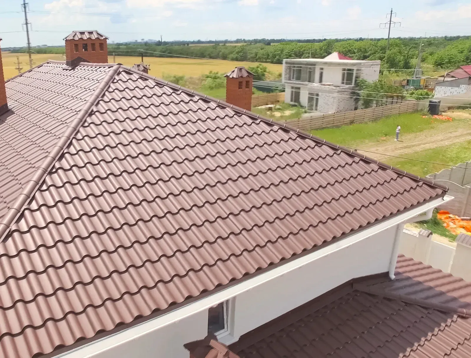 Brown metal roof on a house, with chimney and surrounding landscape.