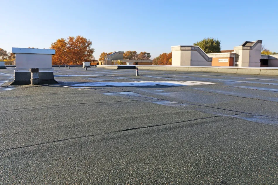 Flat, black, asphalt roof with architectural features under a clear, blue sky.