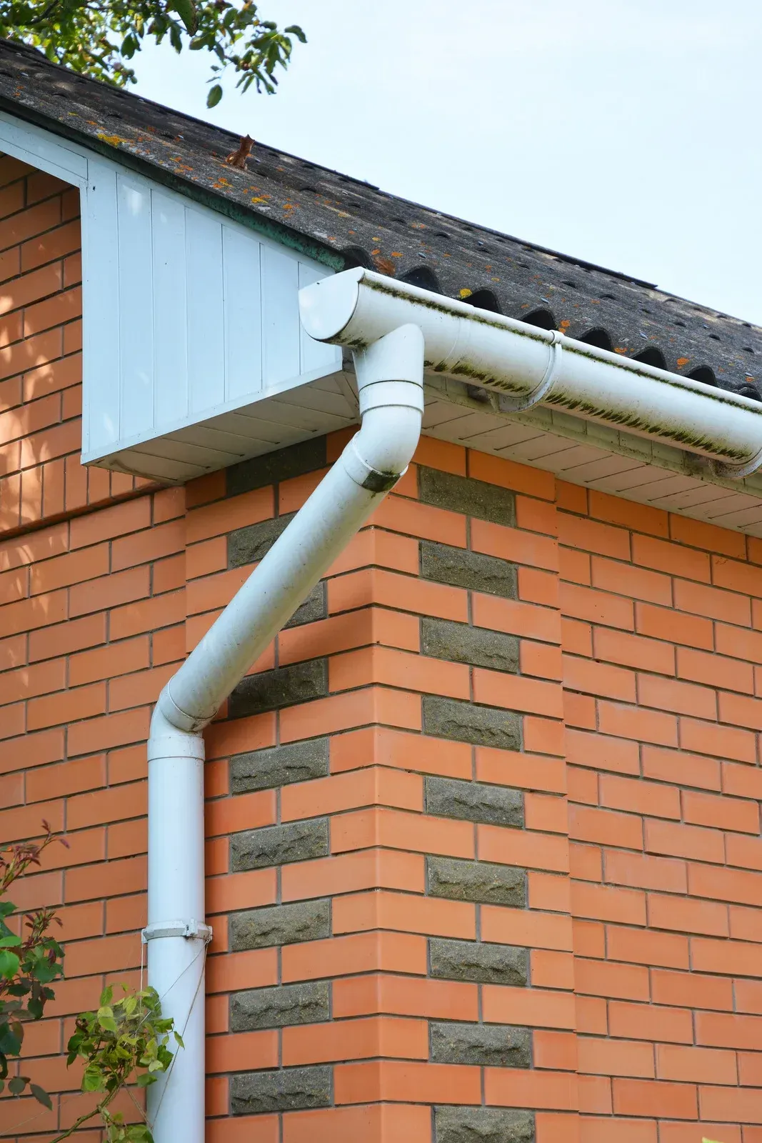 White gutter and downspout on a brick building corner.