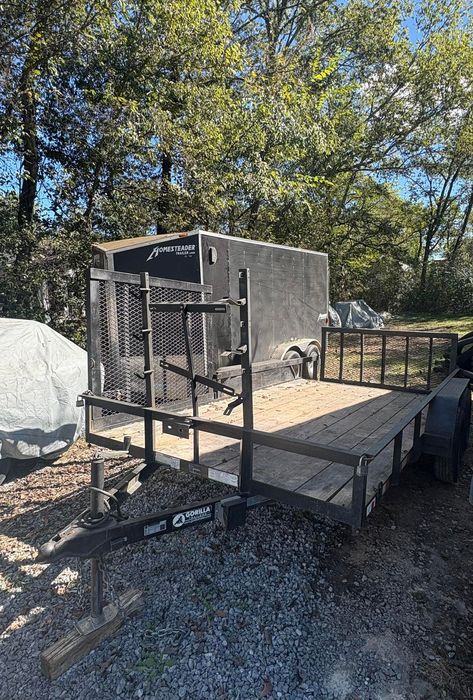 Black utility trailer with wire mesh sides, parked outdoors.
