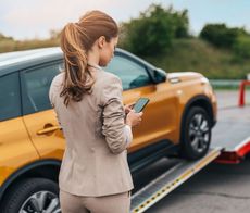 A woman is standing next to a tow truck looking at her phone.