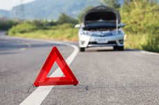 A red triangle is sitting on the side of the road next to a broken down car.