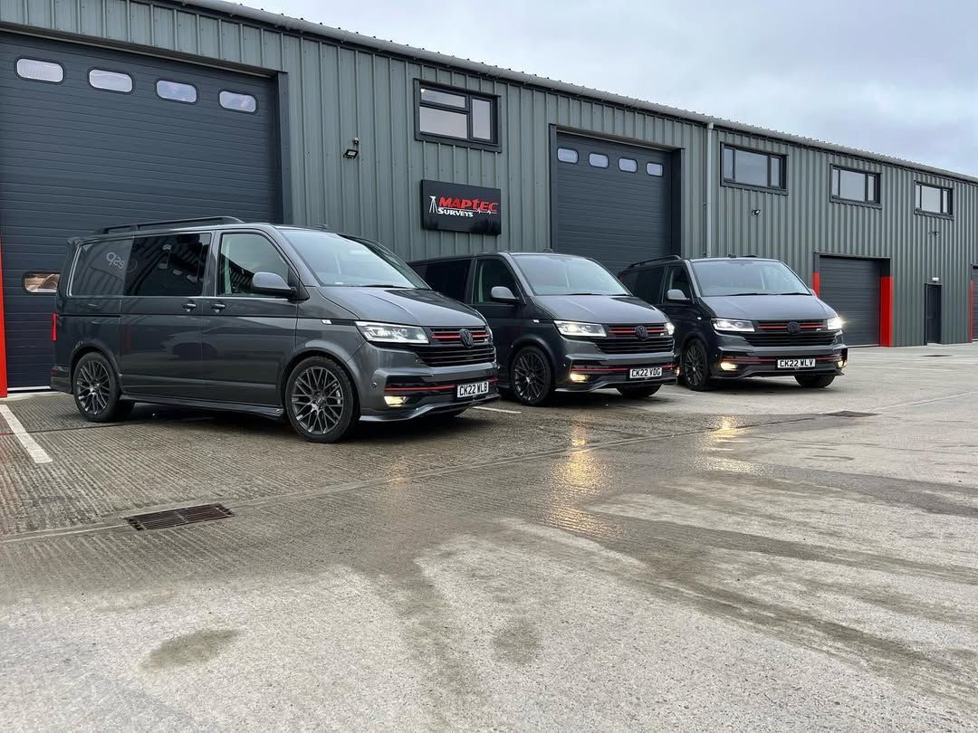 Three gray vans parked in front of a building with garage doors.