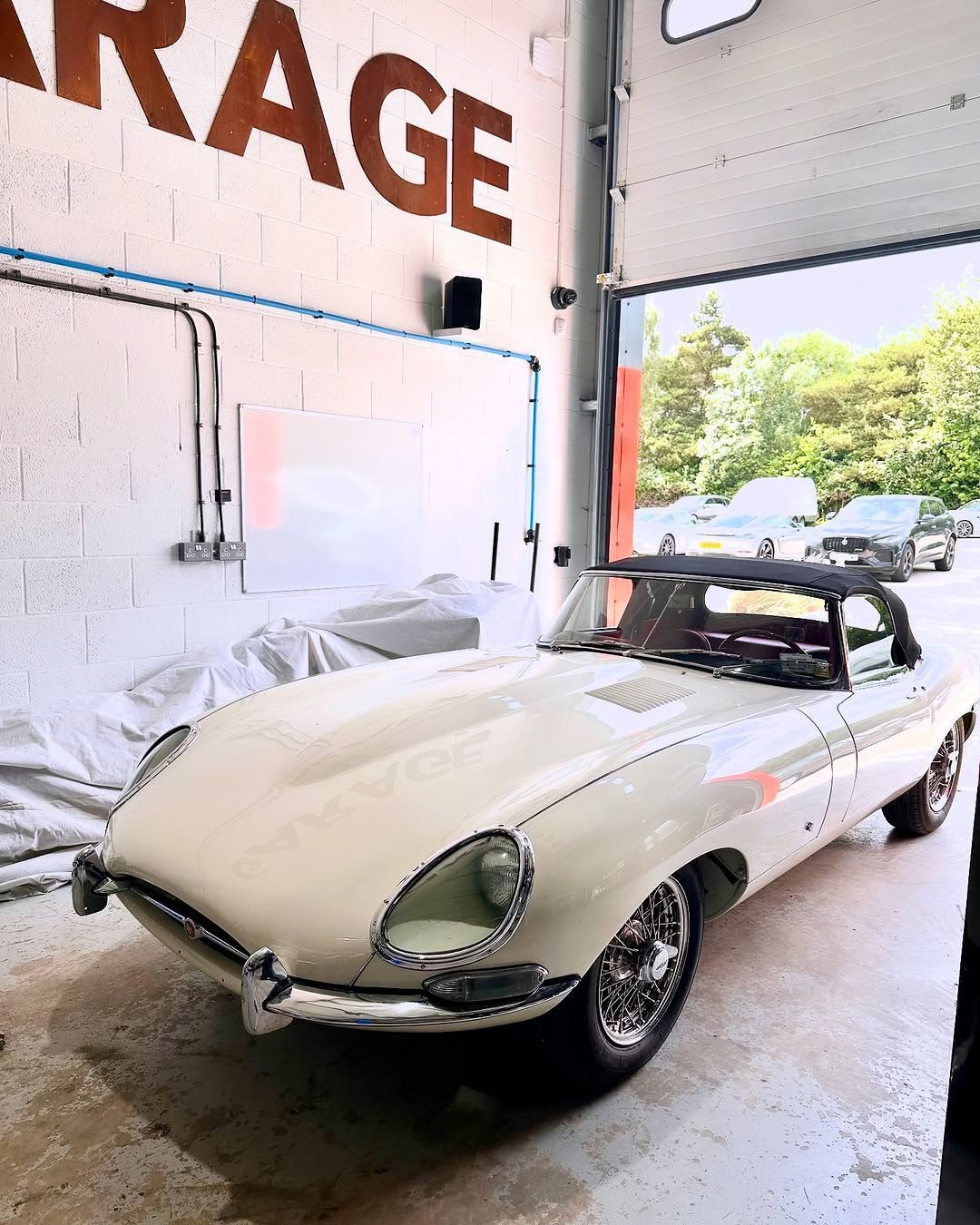 White vintage Jaguar E-Type convertible in a garage, next to an open door.