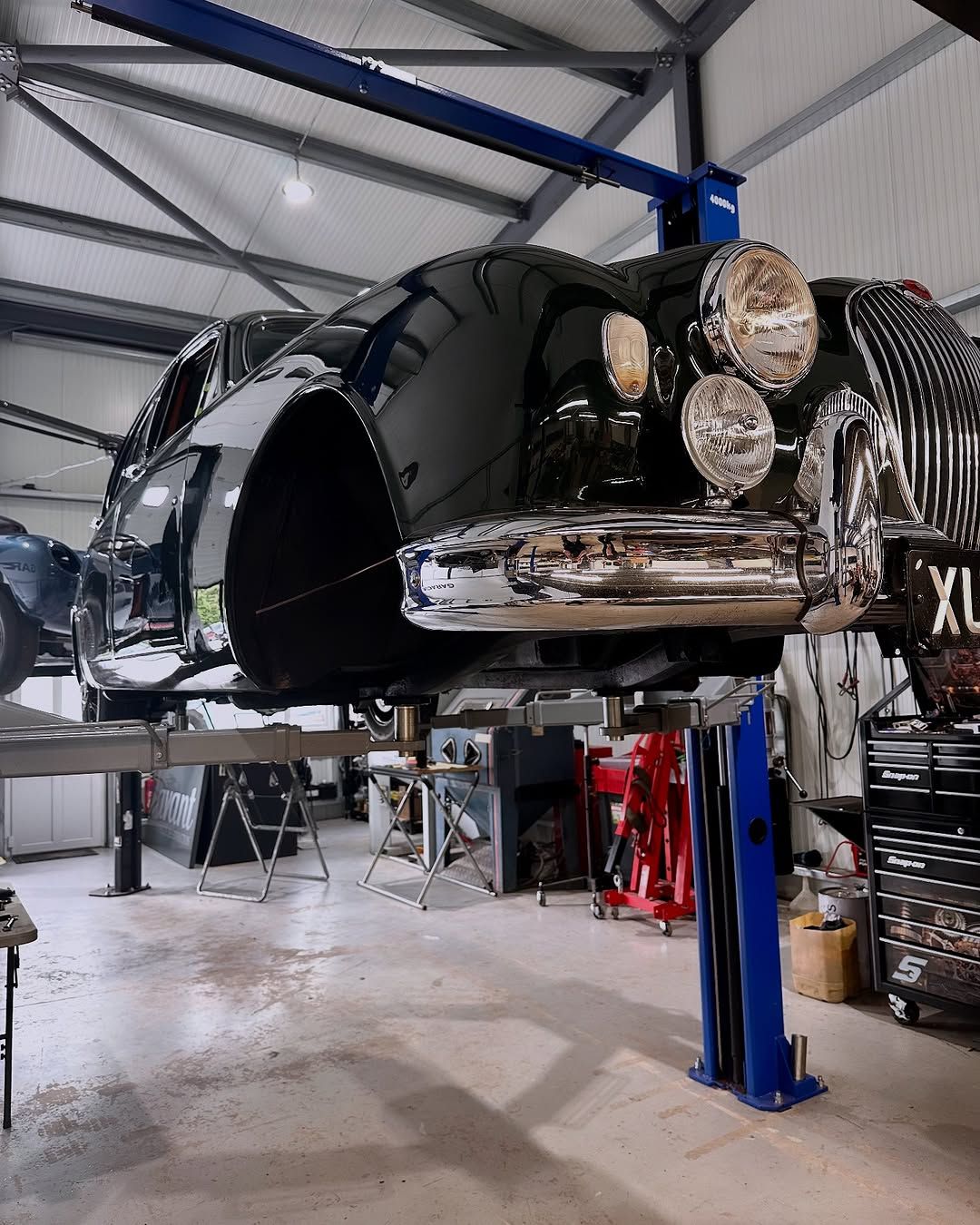 Black classic car on a blue lift in a workshop. Shiny chrome details.