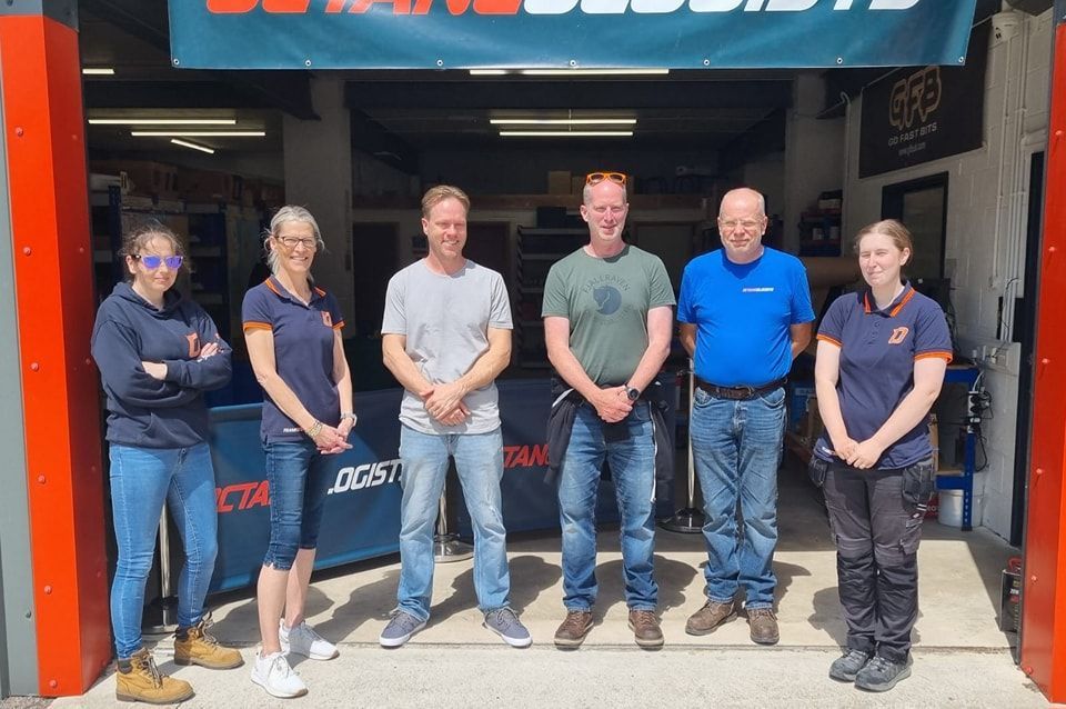 Six people standing outside a business, smiling. Banner above reads