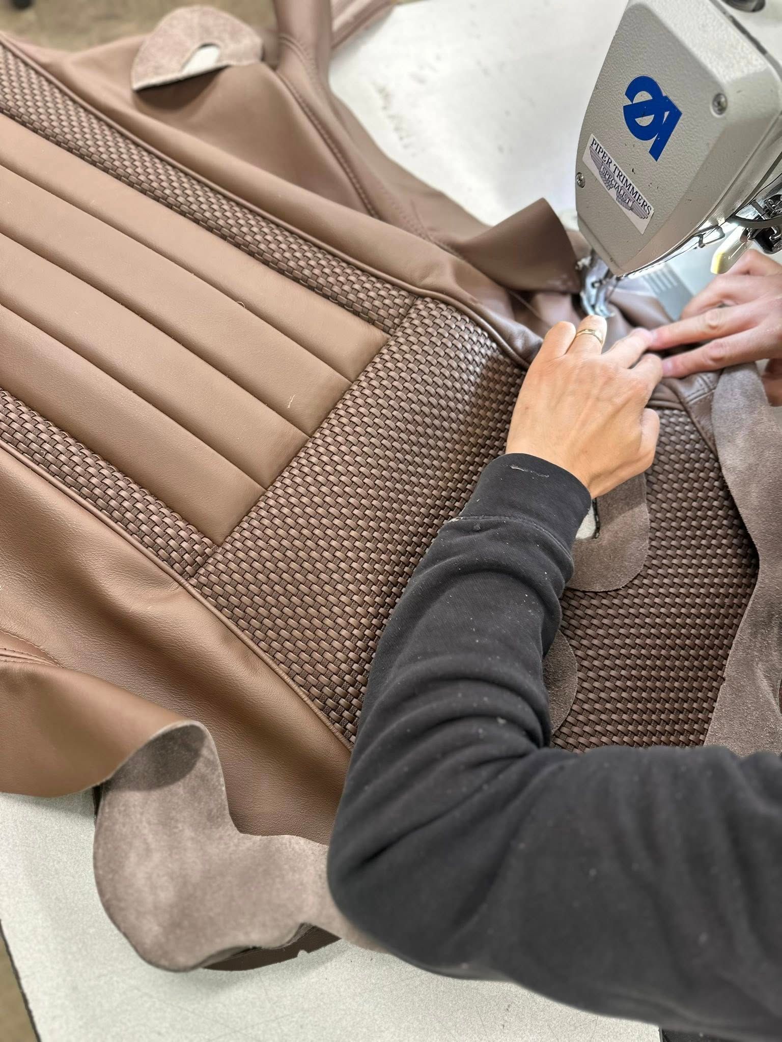 Person using a sewing machine to stitch together beige and brown fabric for upholstery.