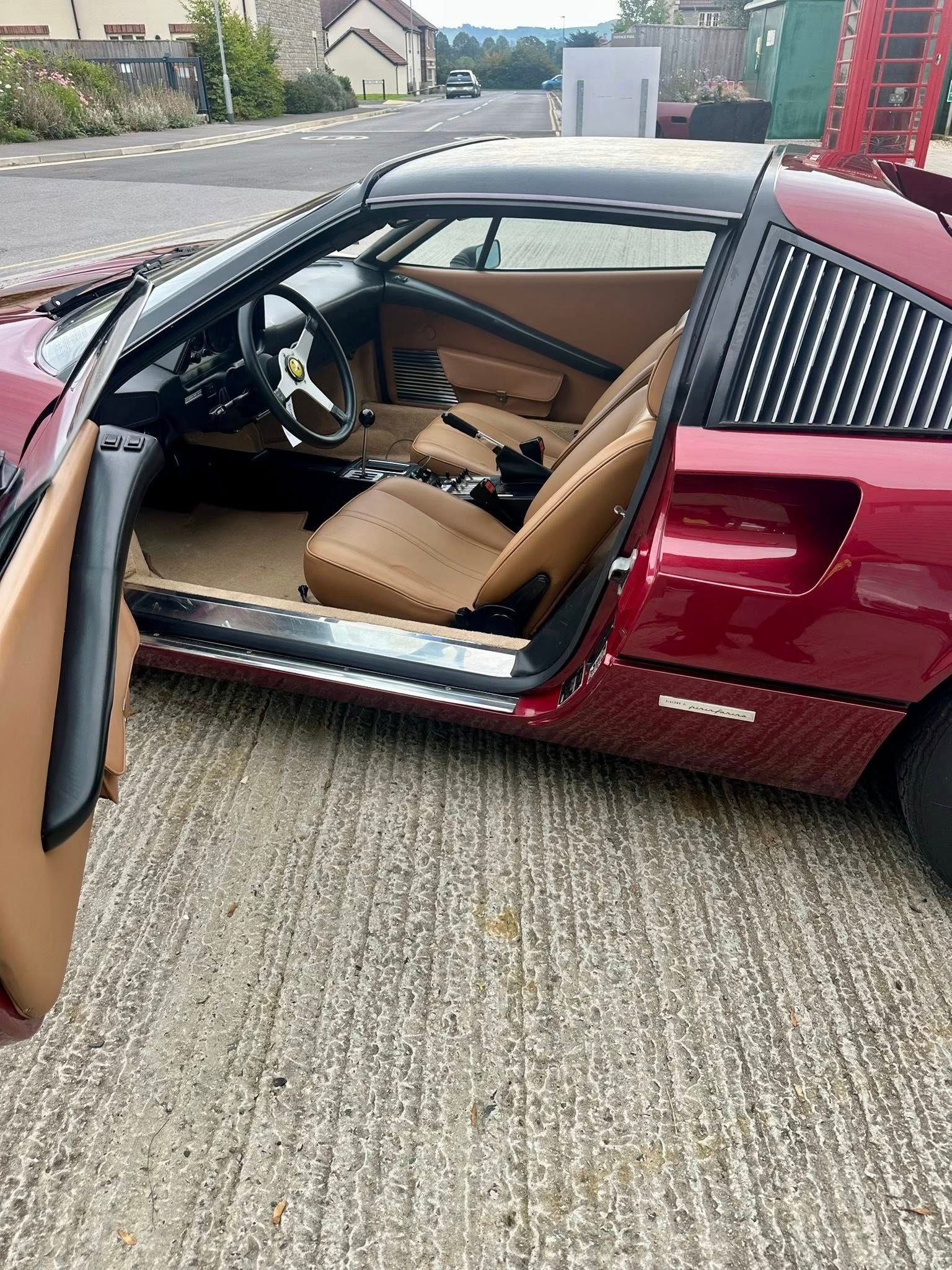 Red Ferrari sports car with open door, tan interior, parked outside.