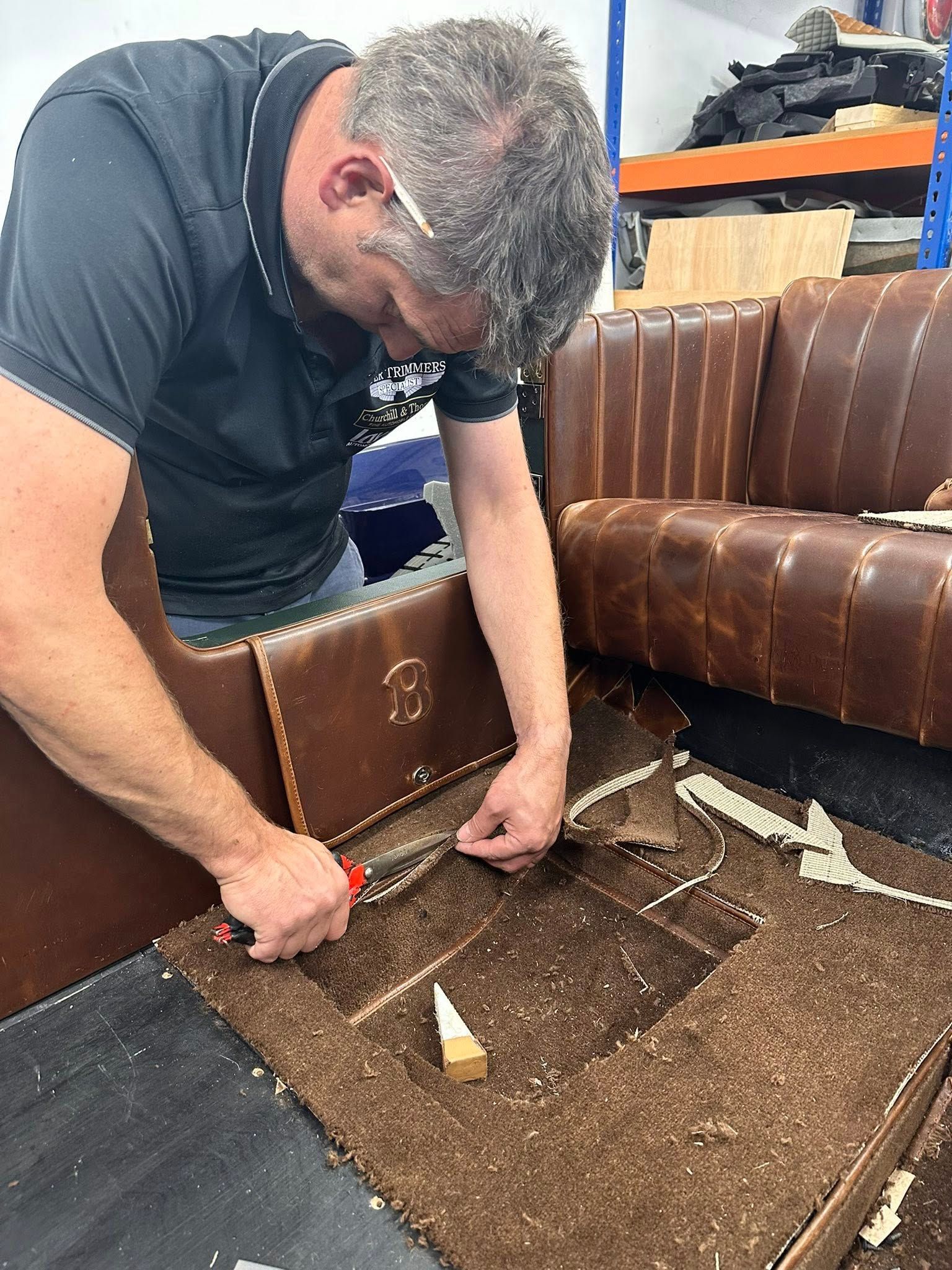 Person working on brown leather upholstery in a workshop. He uses a tool near a sofa.