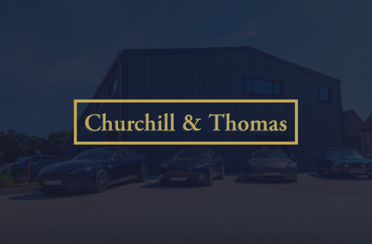 Churchill & Thomas logo over a building and parked cars.