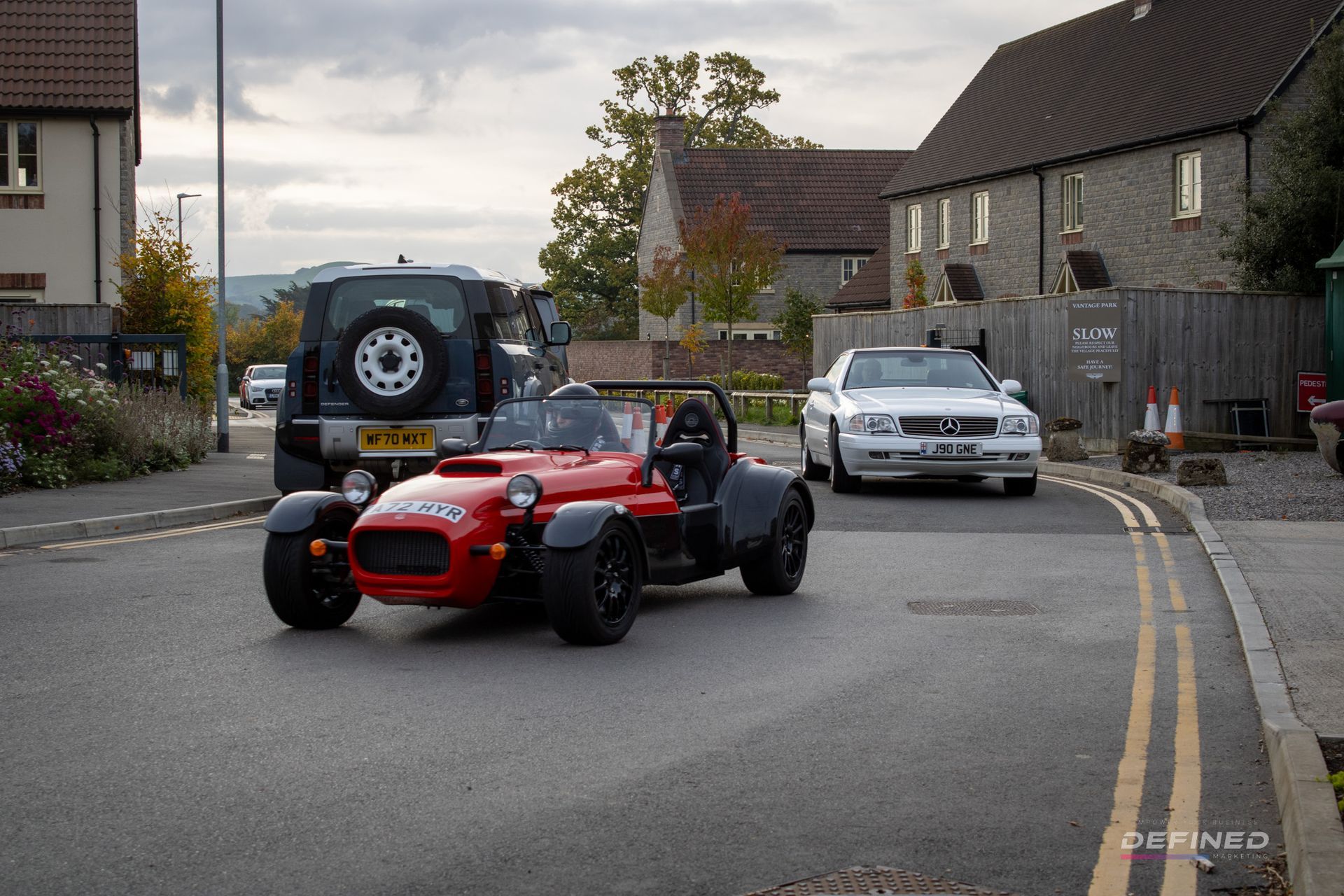 Red sports car on road, other cars and buildings in background. Cloudy day.