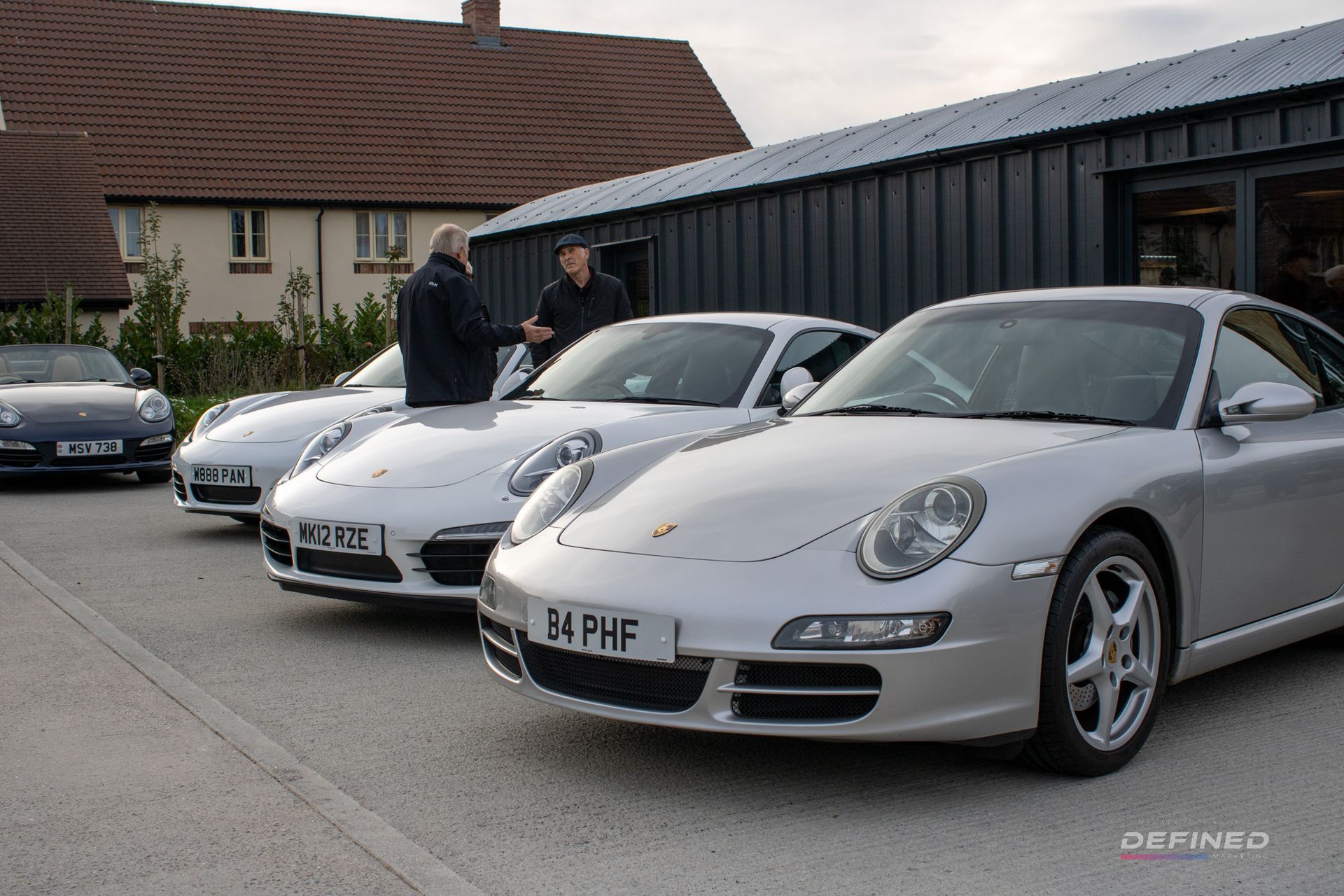 Silver Porsche cars parked outside a building; two men stand by a car.