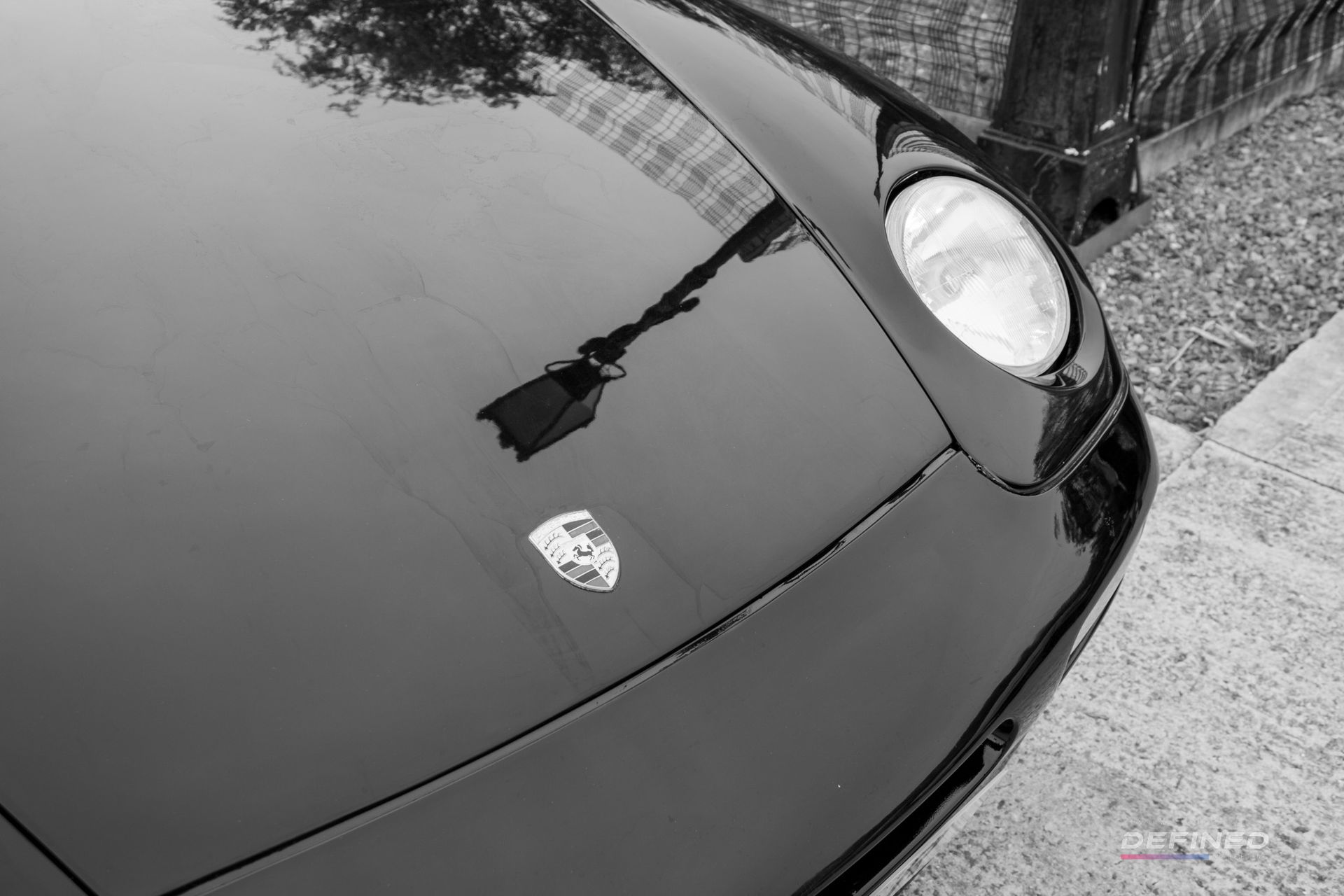 Black Porsche car hood reflecting a street lamp and building, with a Porsche emblem.