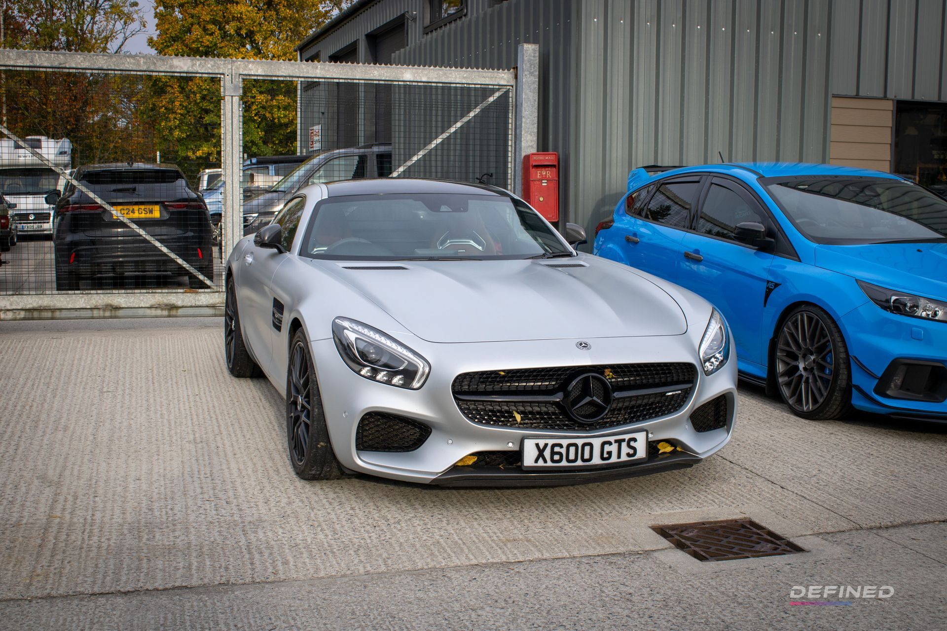 Silver Mercedes AMG GT sports car parked near a blue Ford Focus RS.