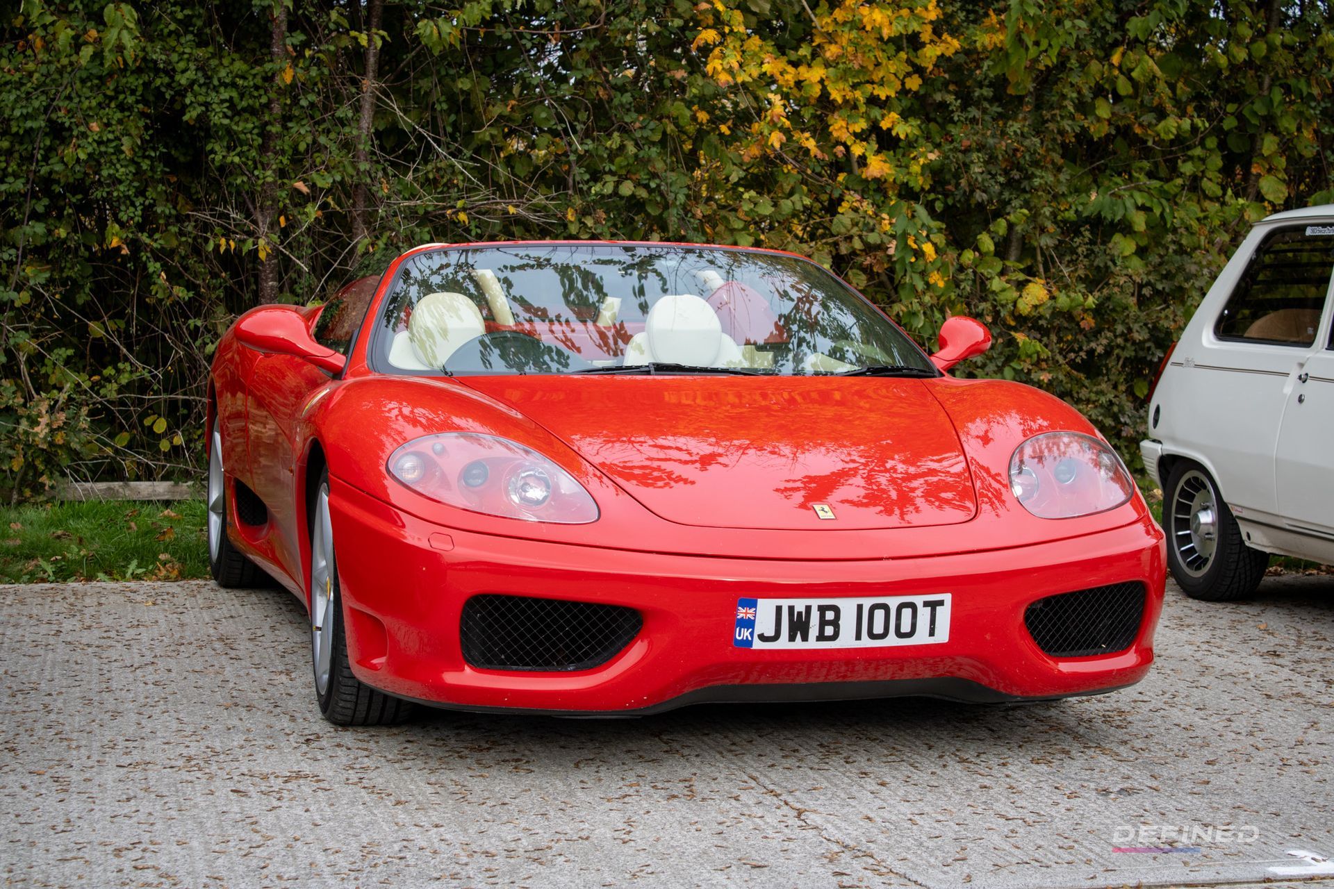 Red Ferrari sports car parked outdoors with trees in the background.