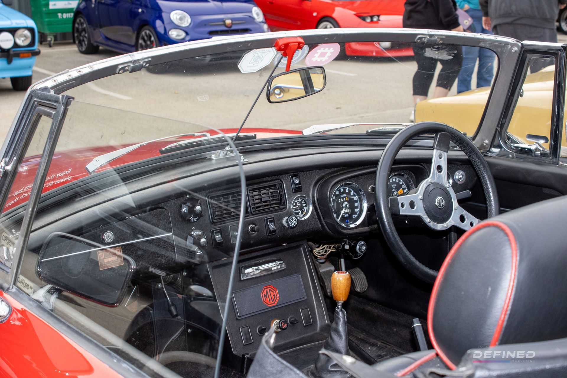 Red convertible car interior, black dashboard, silver steering wheel, exposed gauges.