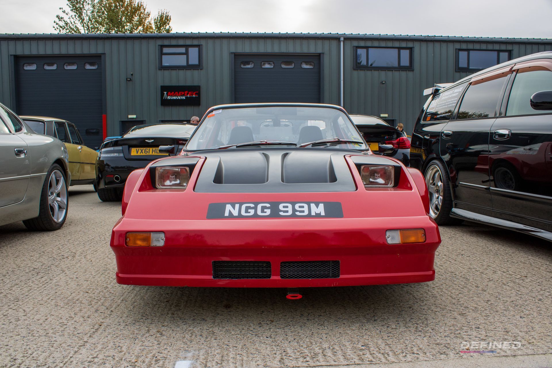 Red car with black hood and pop-up headlights, parked in front of a building.