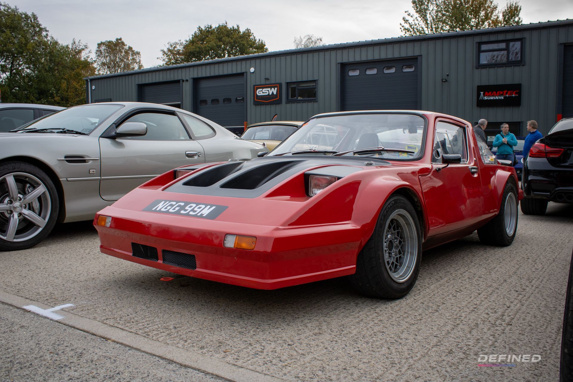 Red sports car with black hood scoop parked outside a gray building.