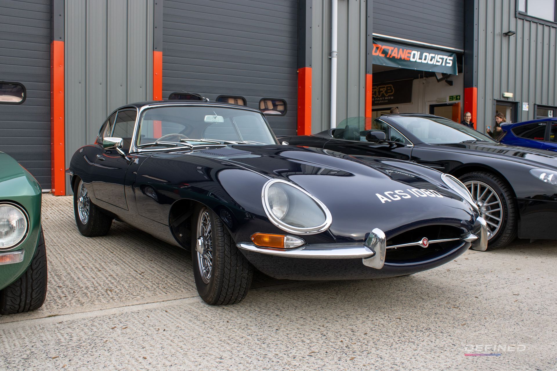 Dark blue Jaguar E-Type coupe parked outside a building, with a silver grille and vintage design.