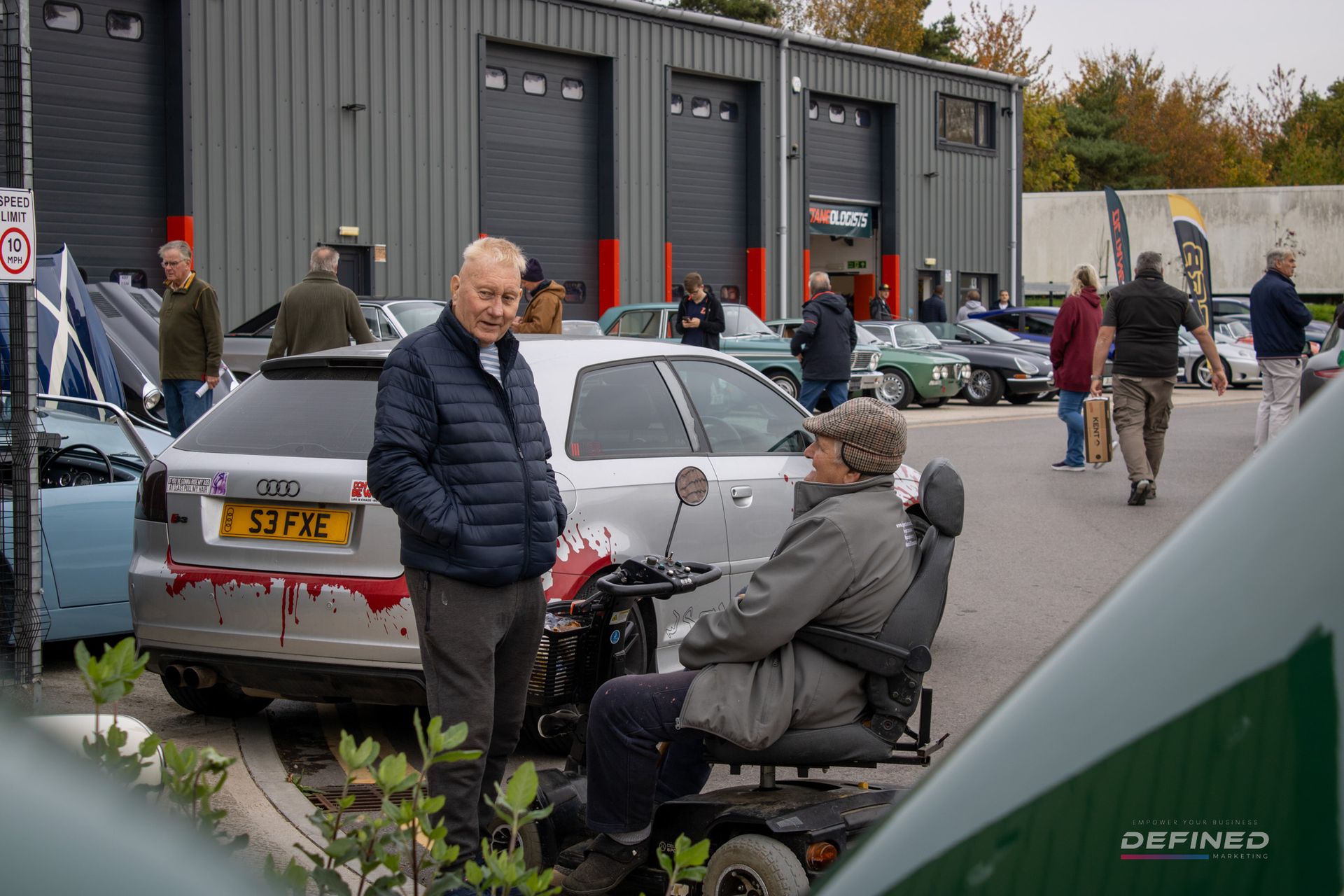 People at a car show, one in a wheelchair, near an Audi with 