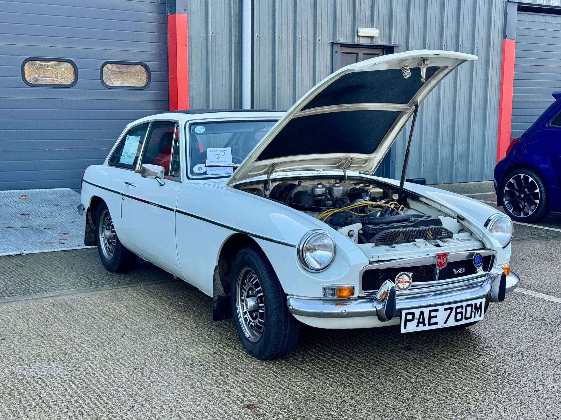 Green vintage Alfa Romeo car parked in front of a gray garage door, with other classic cars on each side.