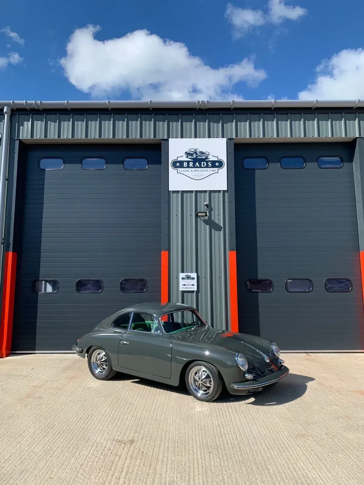 Gray vintage Porsche parked in front of a gray garage with the name