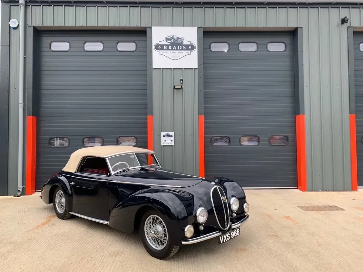 Black vintage convertible car parked in front of a gray garage with red accents.