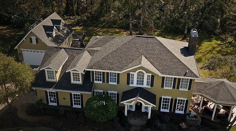 An aerial view of a large yellow house with a black roof