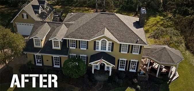 An aerial view of a large yellow house with a black roof.