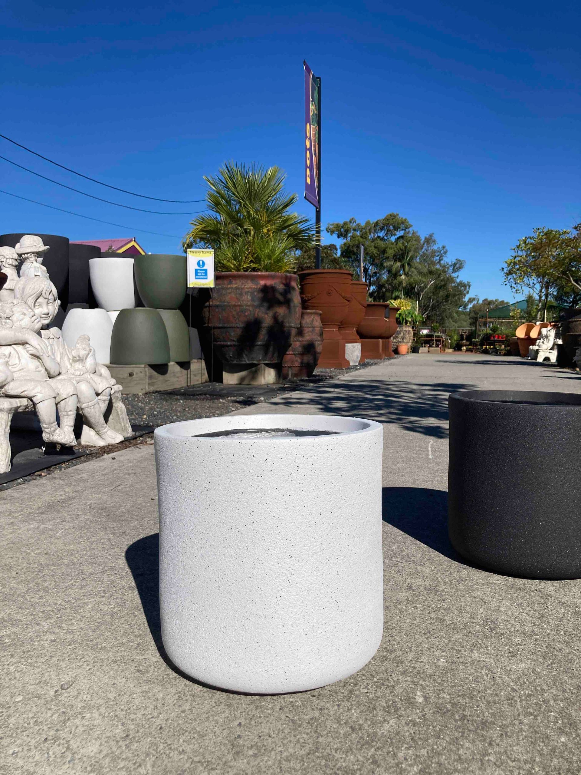 Outdoor display of white and black cylindrical planters in a sunny garden