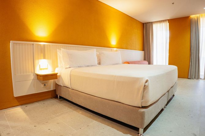 Habitación de hotel en San Andrés con cama doble, muro mostaza, lámparas cálidas y cortinas claras.
