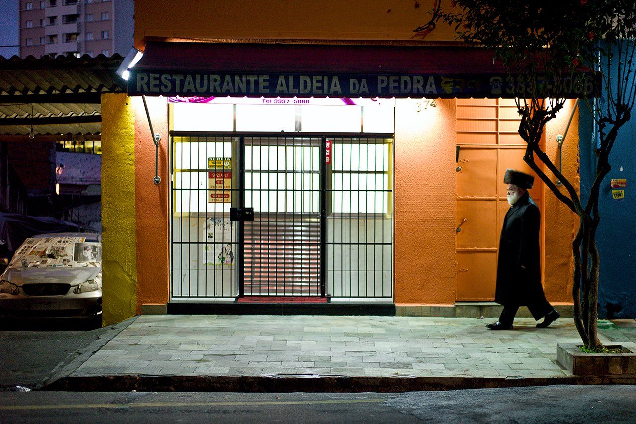Um homem caminhando em frente a um restaurante chamado restaurante aldeia da pedra