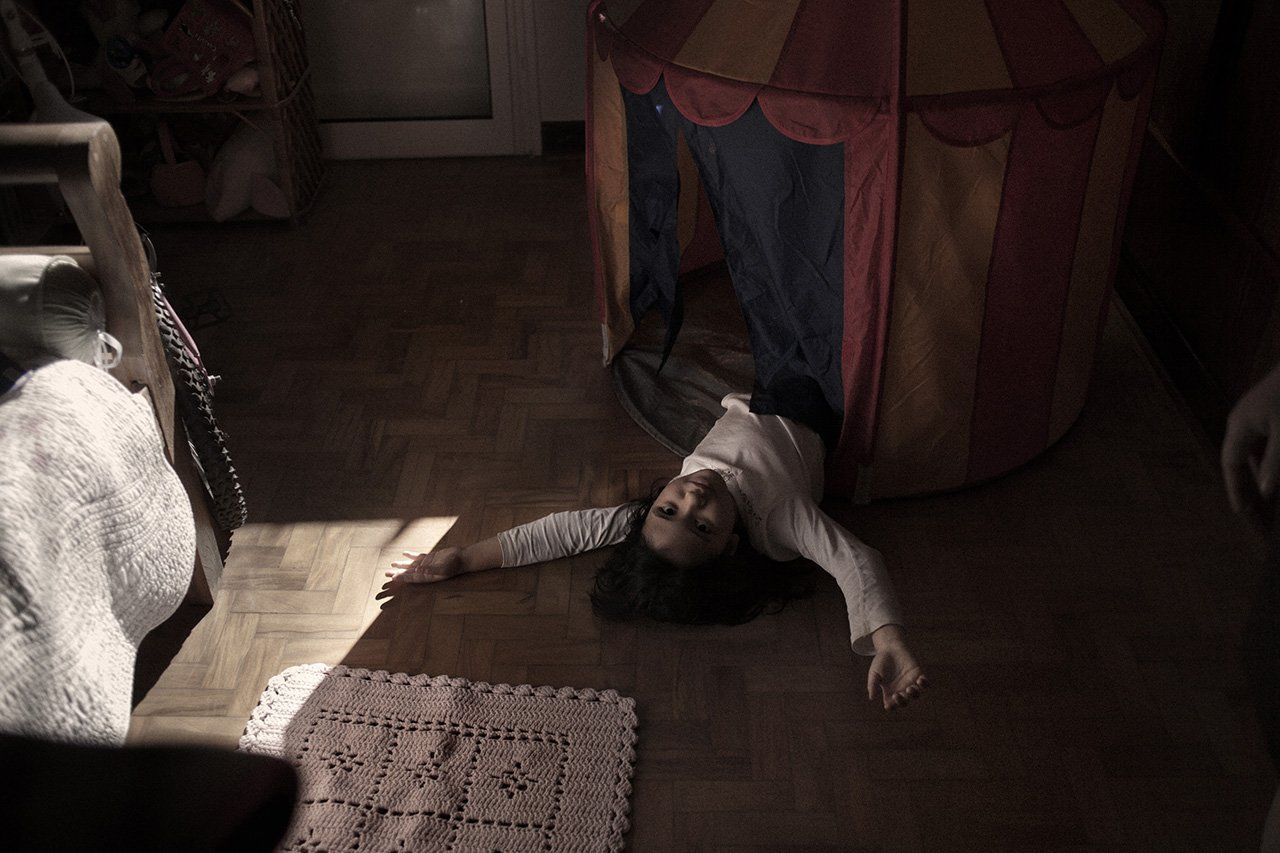 Uma criança está deitada no chão de uma sala ao lado de uma barraca.