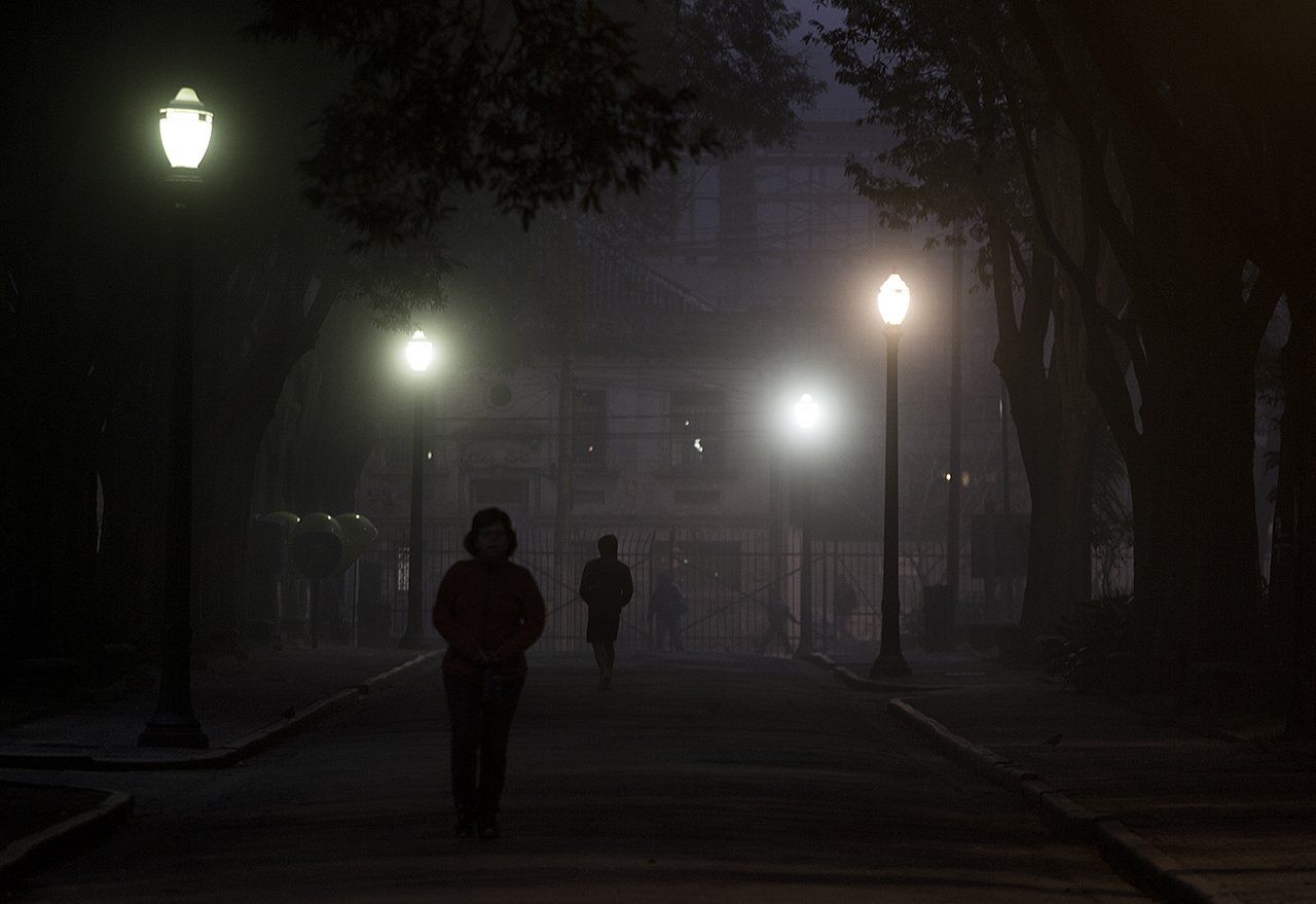 Algumas pessoas estão andando por uma rua enevoada à noite.