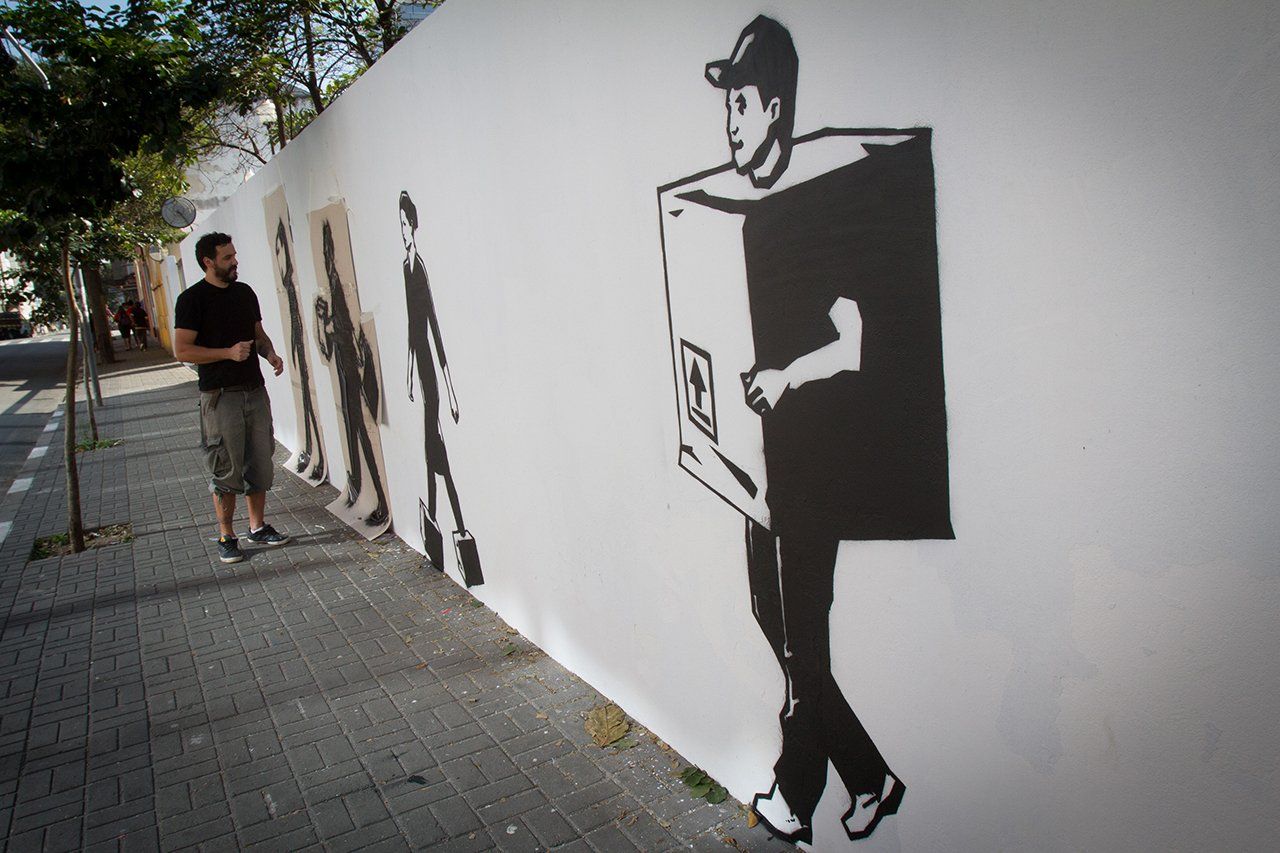 Um homem está parado em frente a uma parede com o desenho de um homem carregando uma caixa nas costas