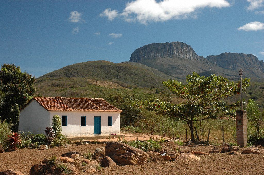 Uma pequena casa branca no meio de um campo com montanhas ao fundo