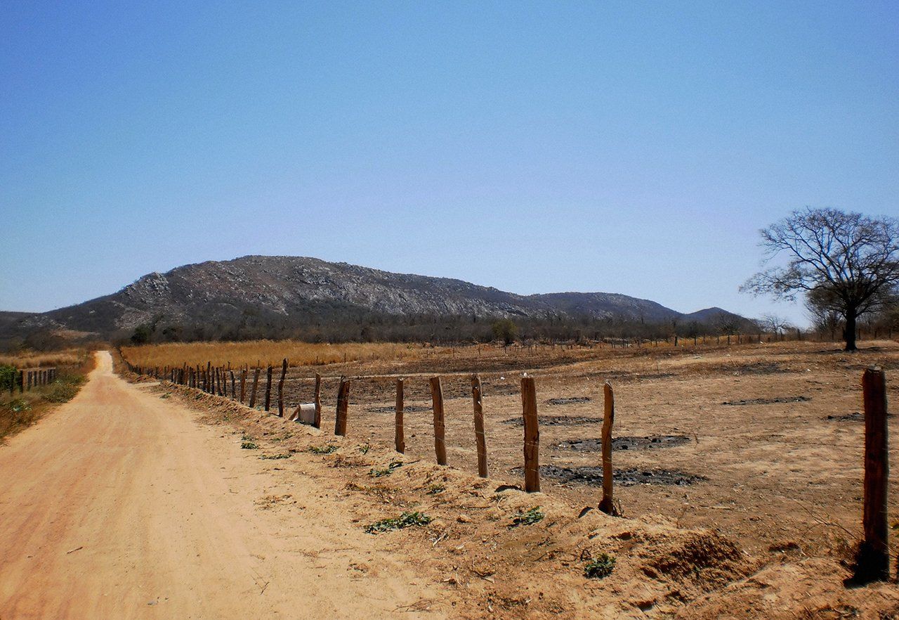 Uma estrada de terra com uma cerca e montanhas ao fundo