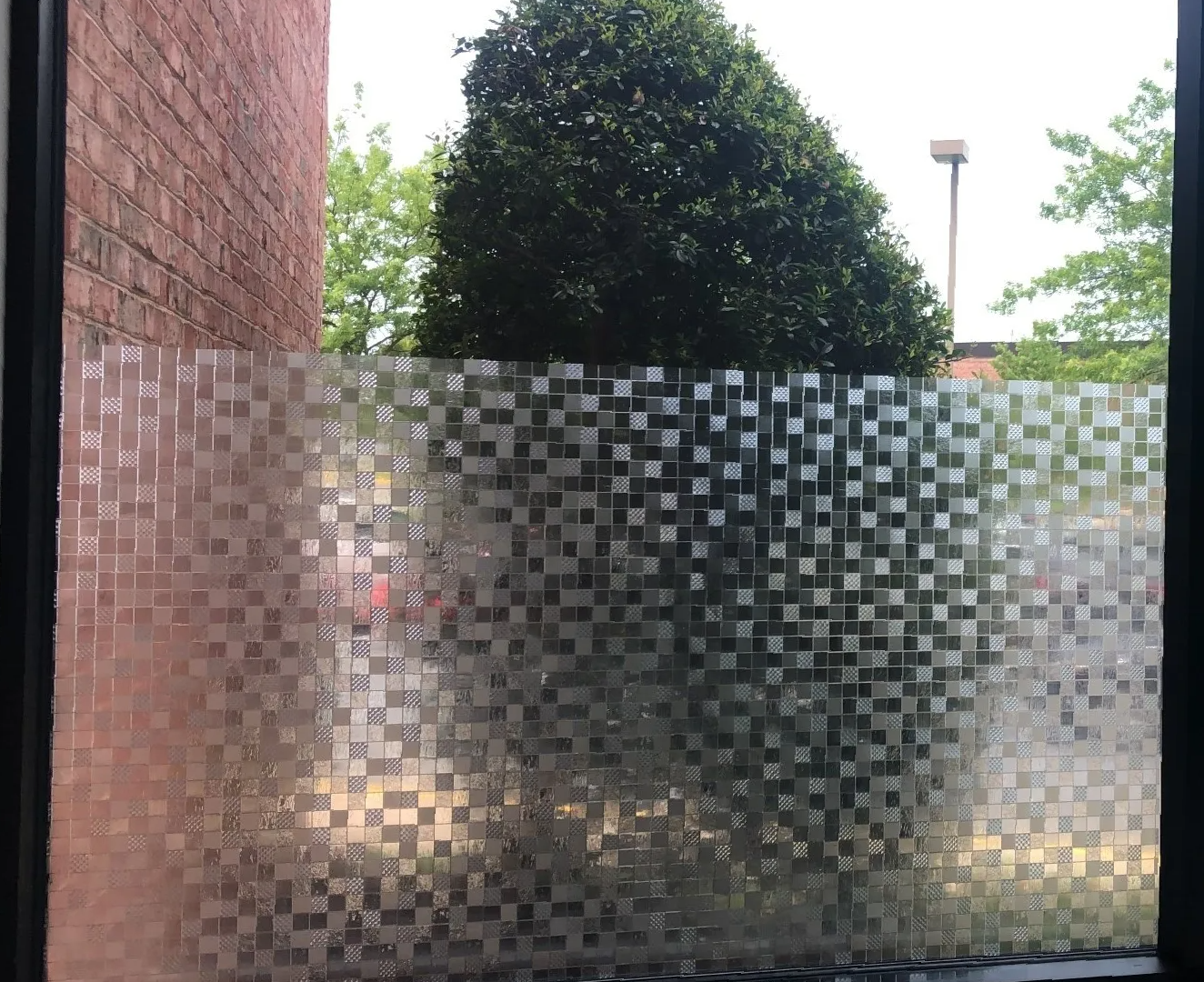 A window with a tree in the background and a brick wall behind it.