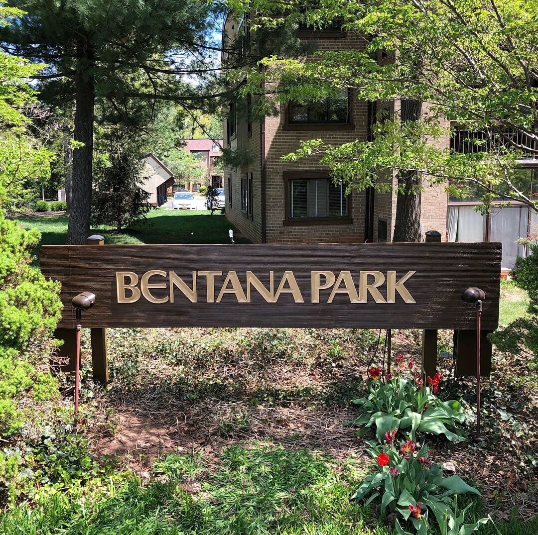 A wooden sign for bentana park is surrounded by trees and bushes.