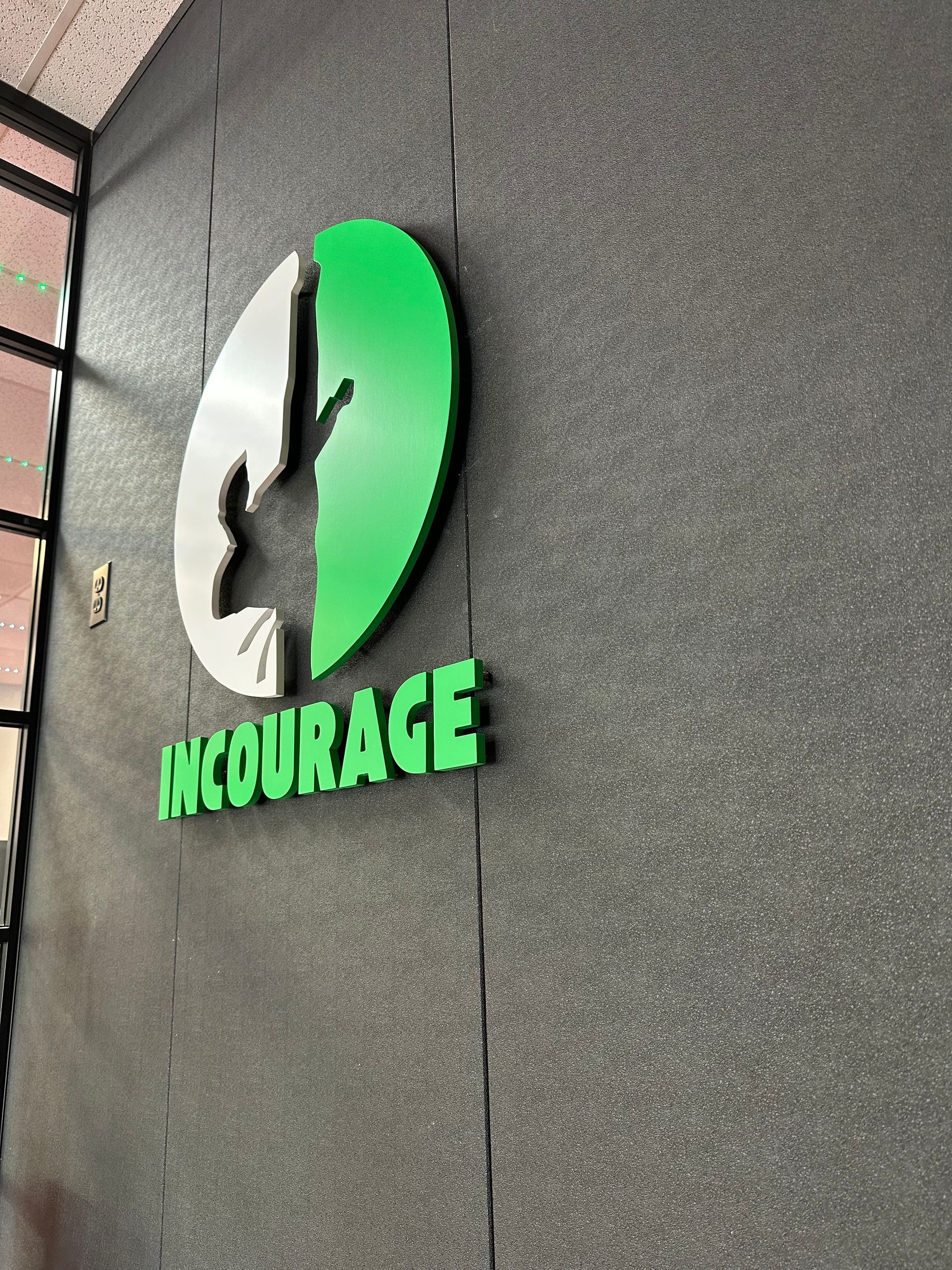 A green and white sign on a wall that says encourage
