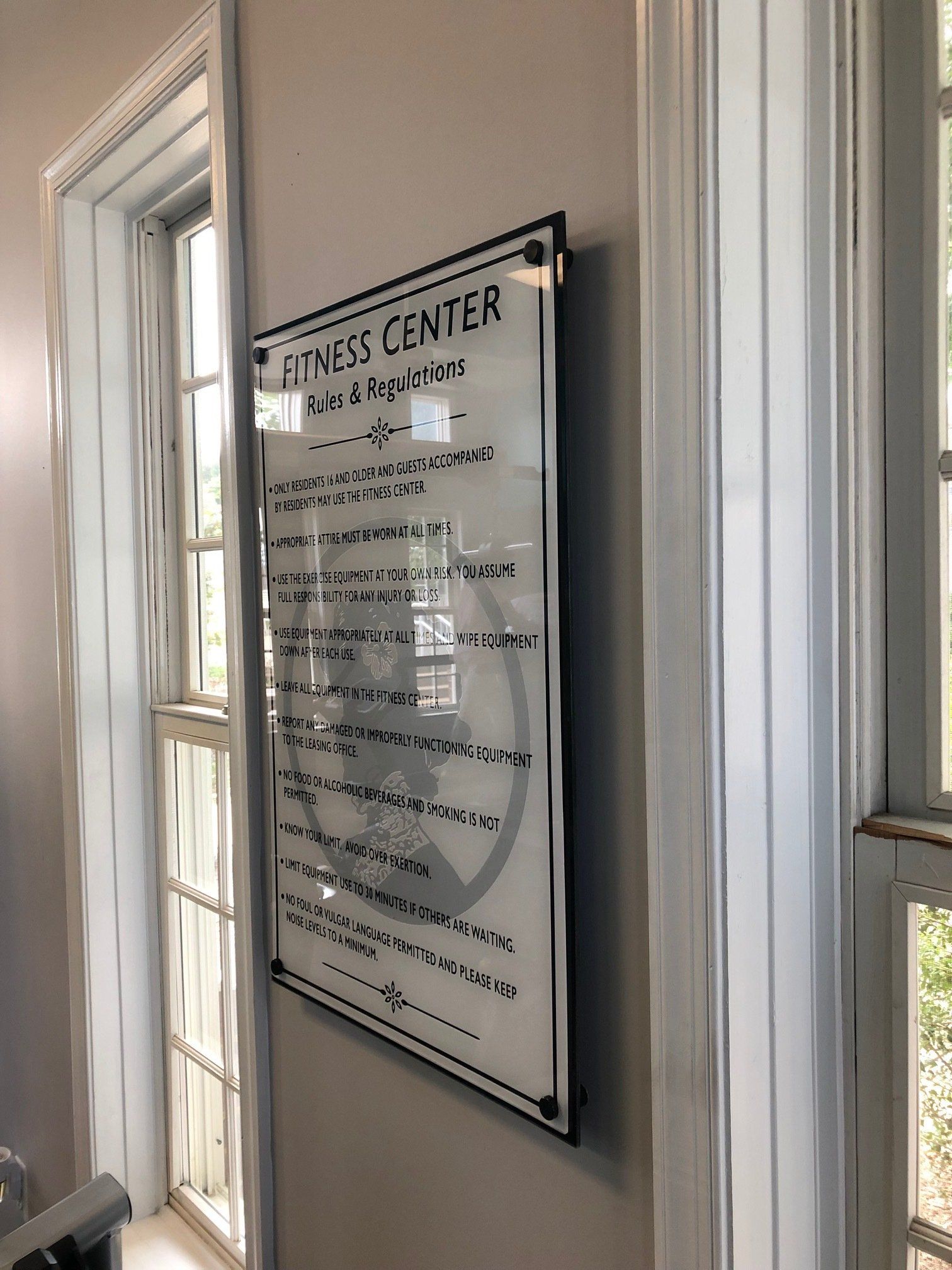 A sign for the fitness center is hanging on a wall next to a window.