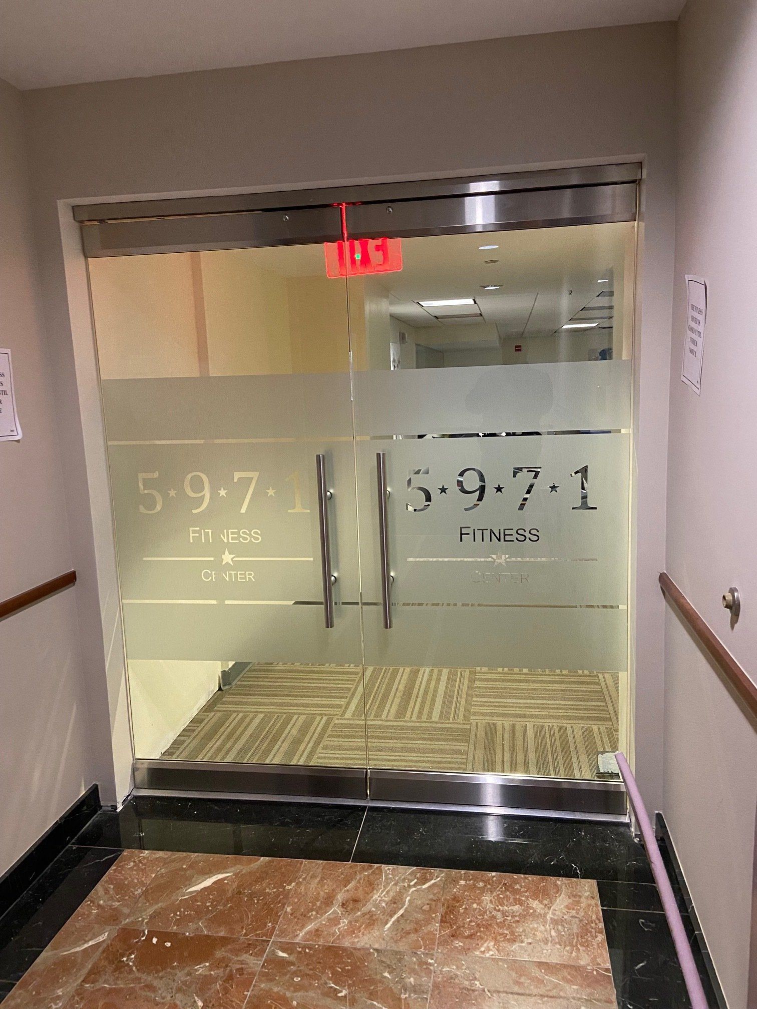 A hallway with a glass door and a red exit sign.