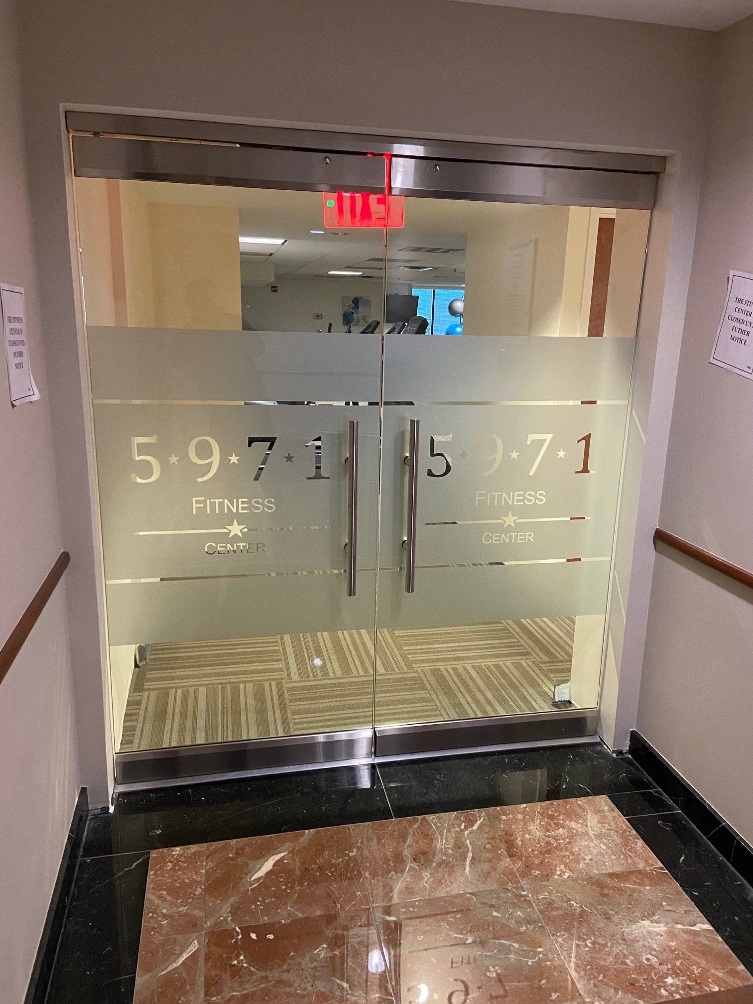 A hallway with a glass door and a red exit sign.