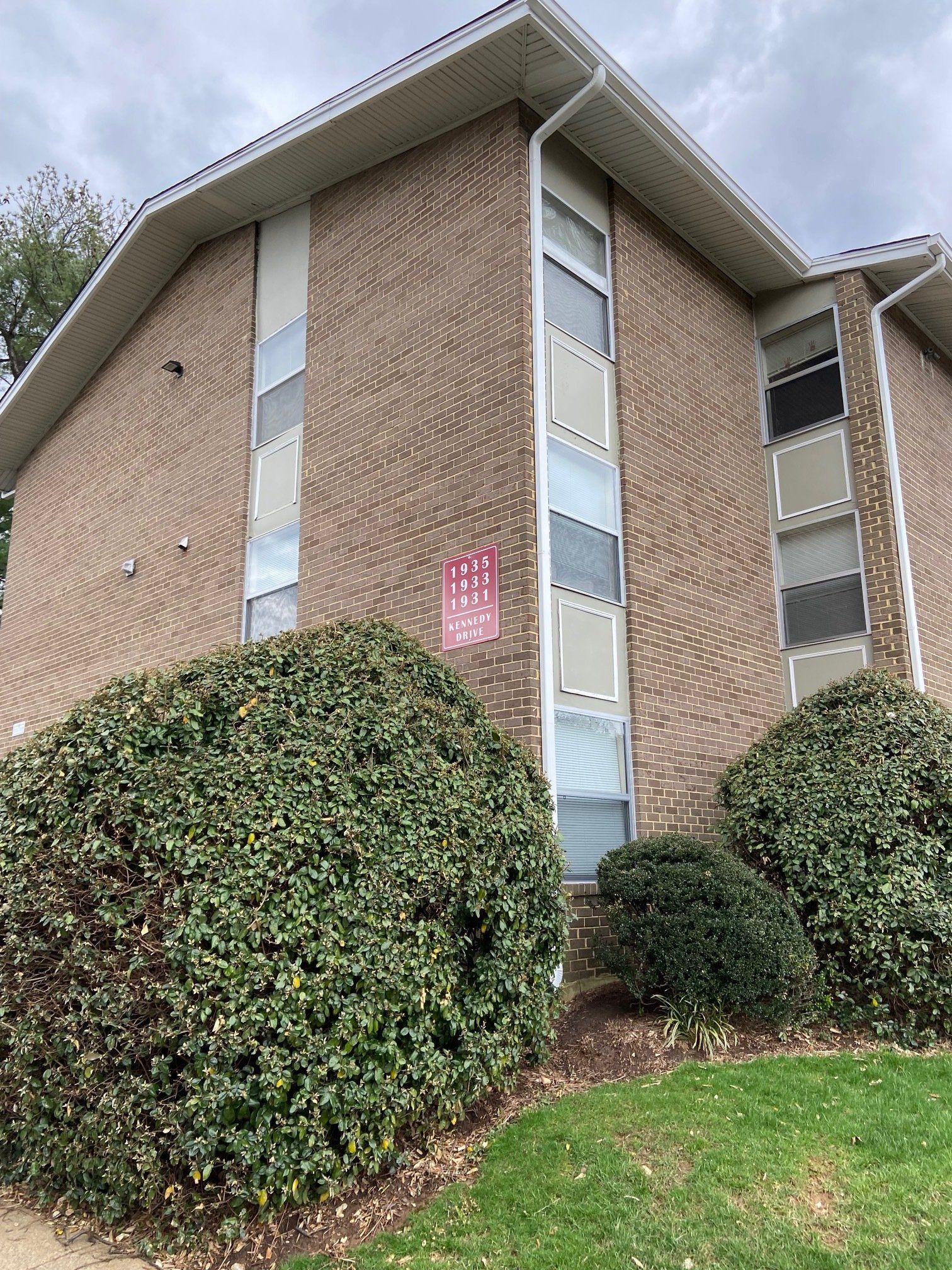 A large brick building with a lot of windows and bushes in front of it.