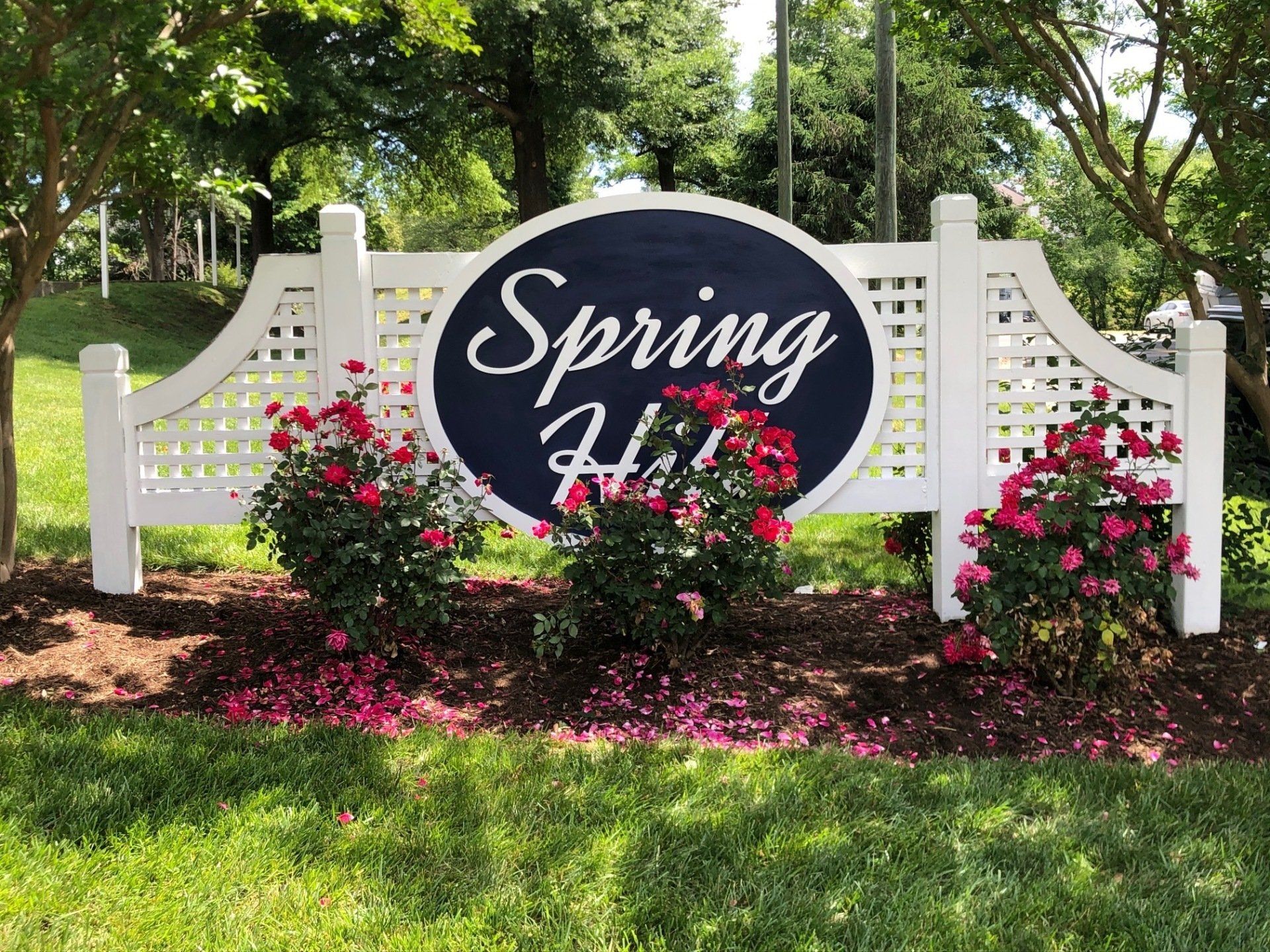A sign for spring hill is surrounded by flowers and trees.