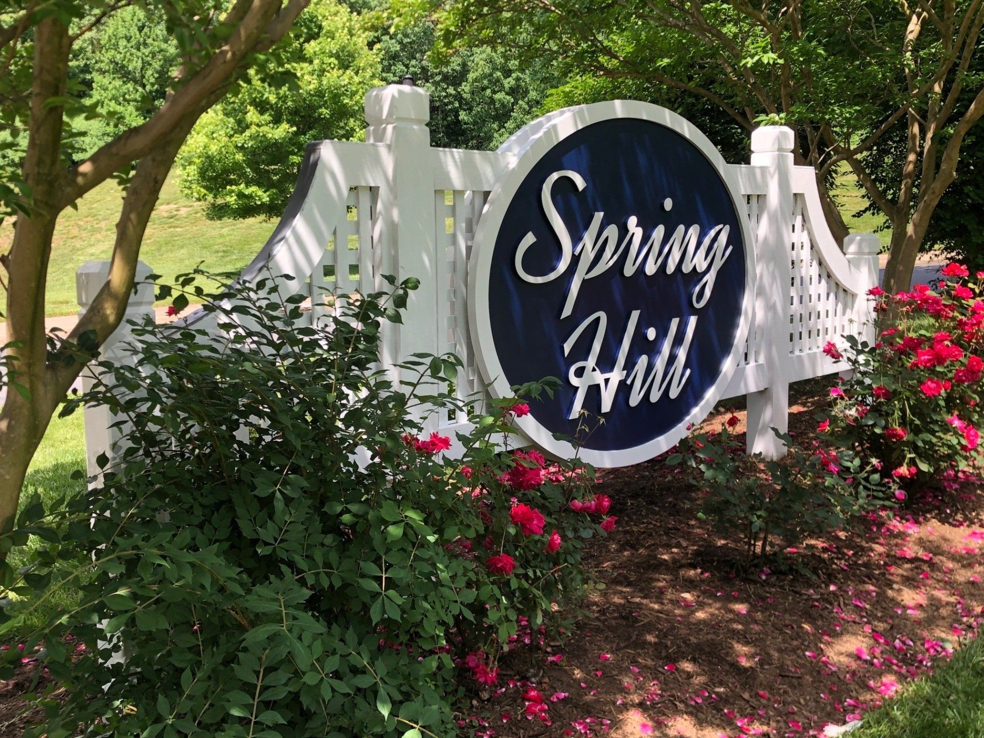 A sign for spring hill is surrounded by flowers and trees.